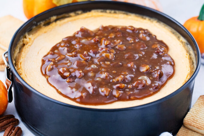Adding pecan caramel topping onto a pumpkin cheesecake.