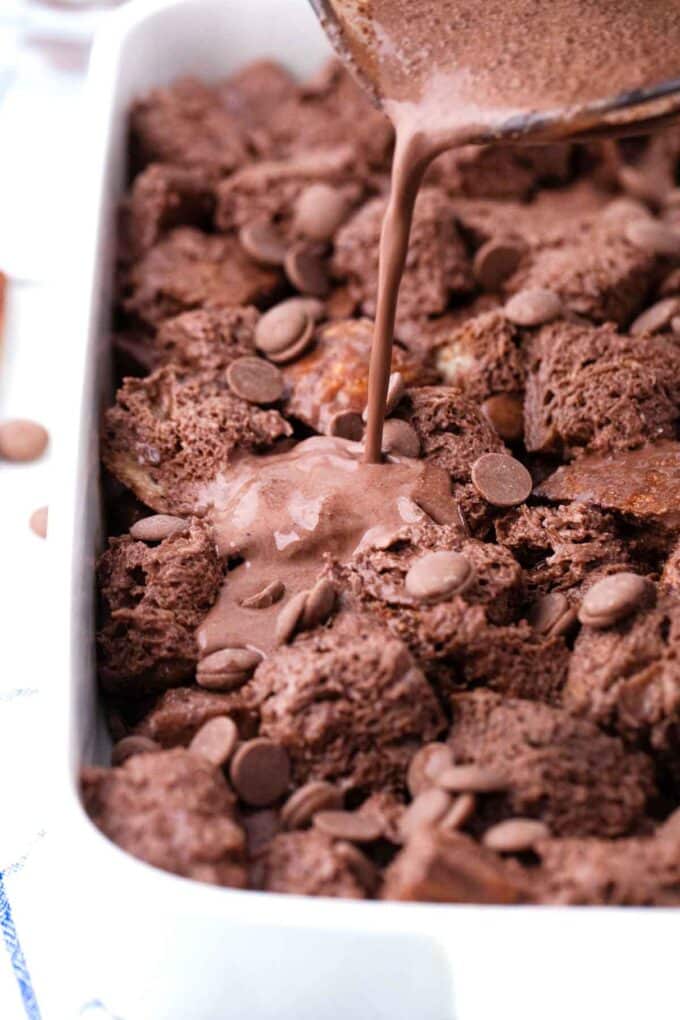 pouring chocolate egg custard over bread pieces in a baking dish