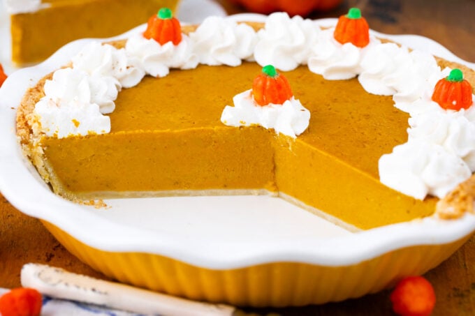 Sliced homemade pumpkin pie topped with whipped cream and candy pumpkins.