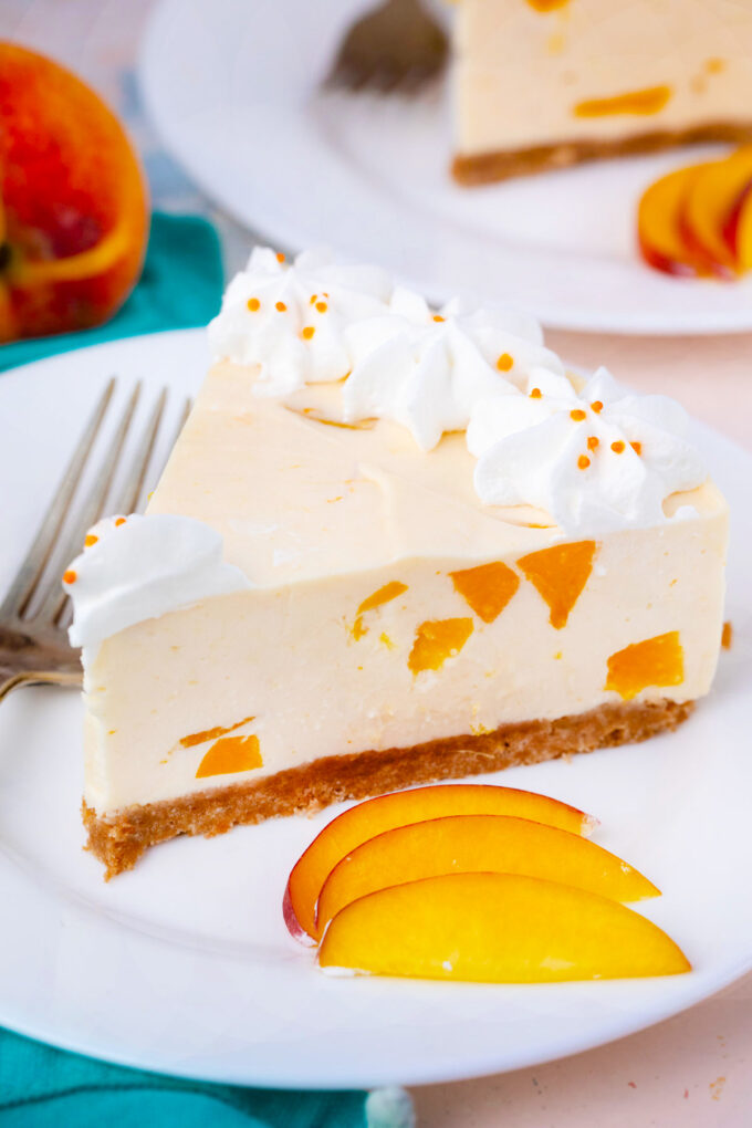 A slice of no bake peach cheesecake topped with whipped cream.