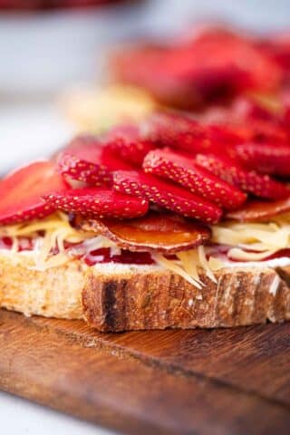 sourdough bread slice topped with cream cheese, strawberry jam, shredded cheddar, crispy bacon, and strawberries