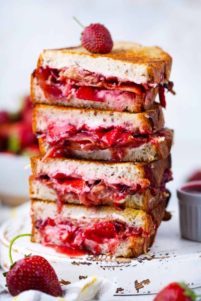 four crispy strawberry bacon grilled cheese sandwiches stacked on top of each other, revealing gooey cheese, juicy strawberries, and crispy bacon