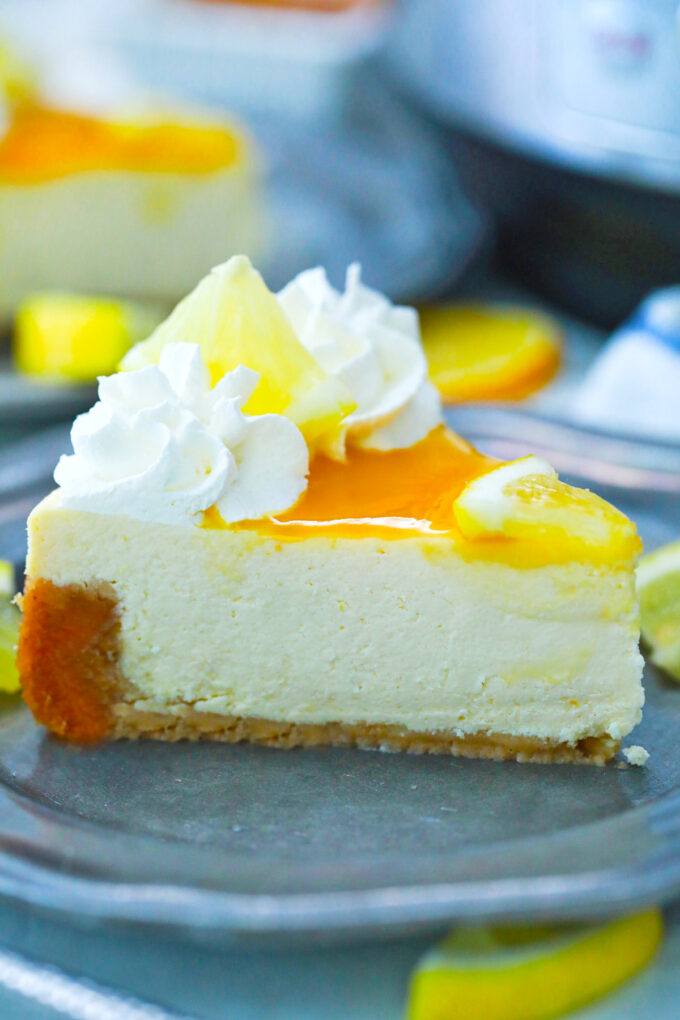 Instant Pot Meyer lemon cheesecake topped with lemon curd, whipped cream, and lemon slices.