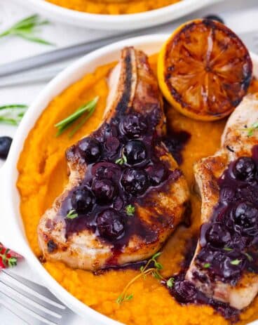 overhead shot of blueberry pork chops topped with blueberry saace and served with a grilled lemon half