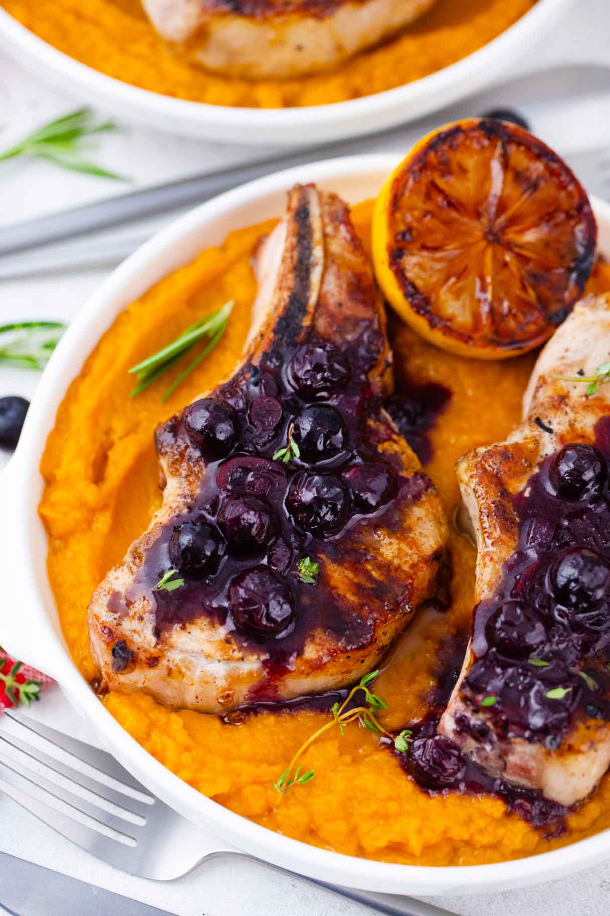 overhead shot of blueberry pork chops topped with blueberry saace and served with a grilled lemon half