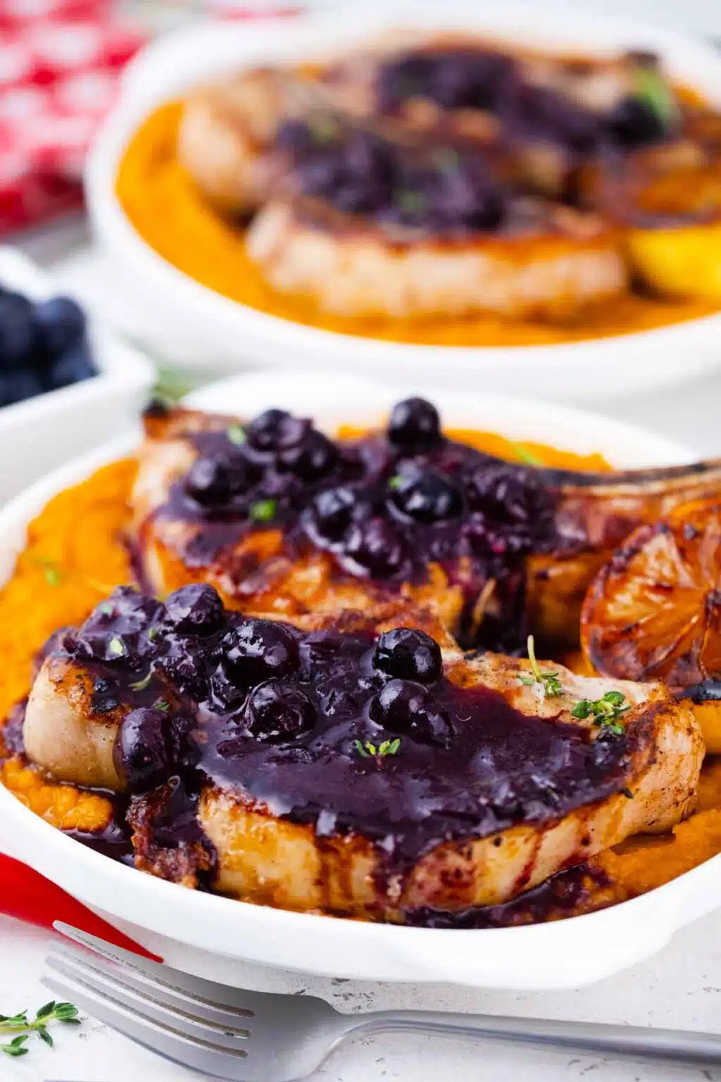 Overhead shot of blueberry pork chops topped with blueberry saace and served with a grilled lemon half.