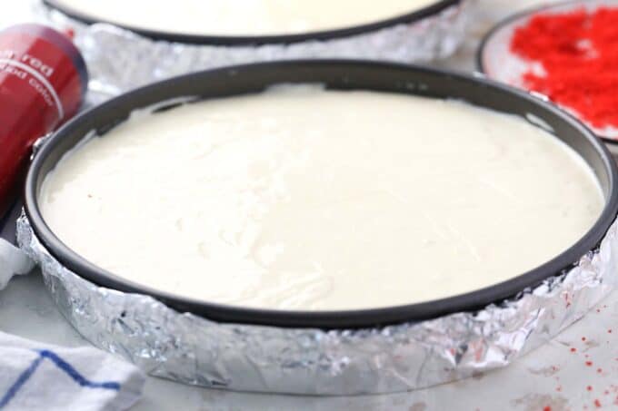 cheesecake batter in two pans covered in aluminum foil