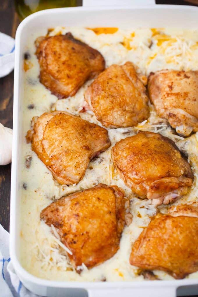 adding browned chicken thighs to creamy mushroom sauce in a casserole dish