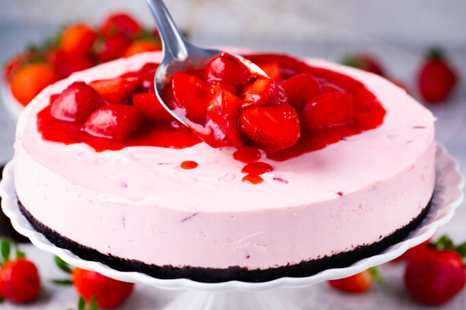 Adding strawberry topping on top of no-bake strawberry cheesecake.