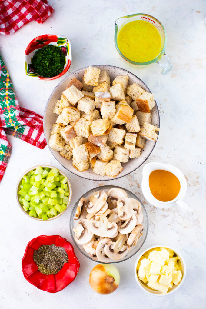 Overhead shot of crockpot stuffing ingredients in bowls on a white surface.