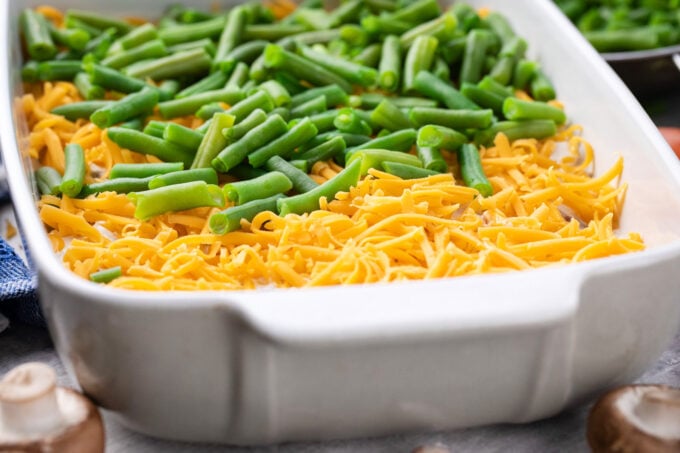 Adding green beans and cheese to homemade tater tot casserole.