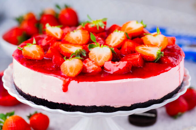 Homemade pink no-bake strawberry cheesecake with strawberry topping and an Oreo crust.