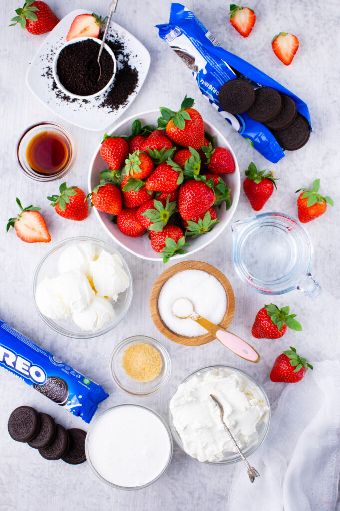 Overhead shot of no-bake strawberry cheesecake ingredients in bowls on a table.