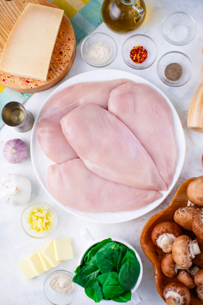 Overhead shot of creamy parmesan mushroom chicken ingredients arranged on a white surface.