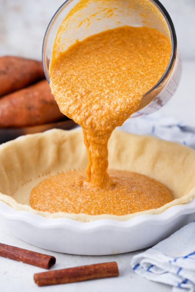 Pouring sweet potato pie filling over homemade pie crust.
