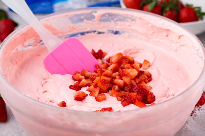 Stirring fresh chopped strawberries into cheesecake batter.