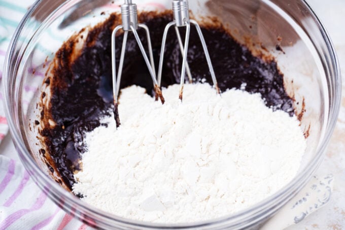 Mixing dry ingredients into wet ingredients for chocolate crinkle cookies.