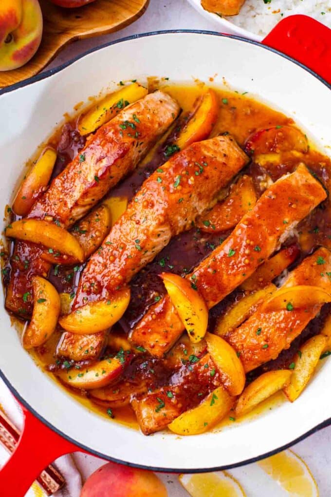 overhead shot of peach salmon in a skillet in a thick sauce topped with peach slices