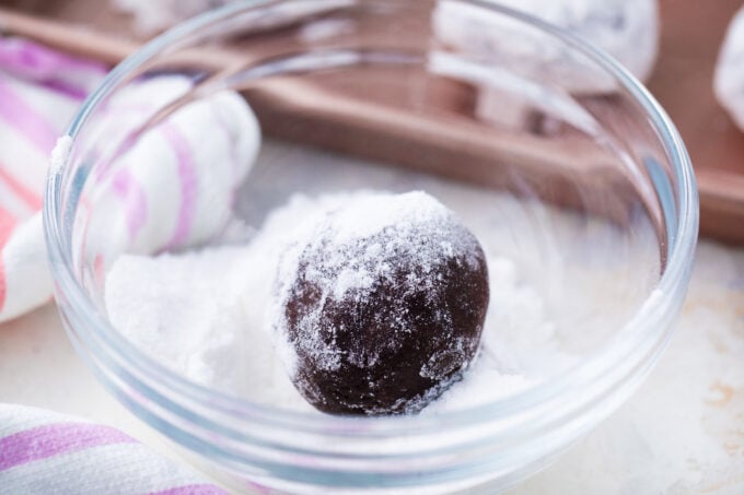 Rolling chocolate crinkle cookies in powdered sugar.