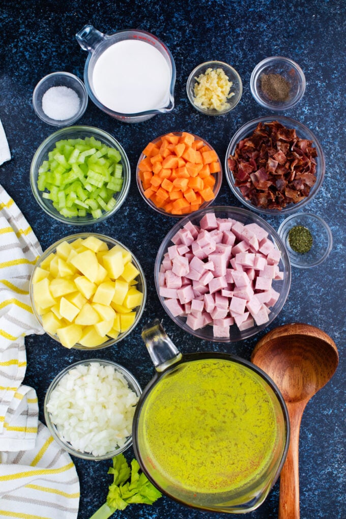 Overhead shot of slow cooker ham and potato soup ingredients in bowls on a dark table.