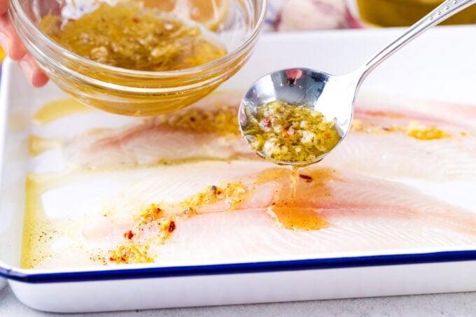 Drizzling tilapia fillets with lemon garlic sauce.