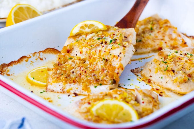 Lifting a baked lemon garlic tilapia fillet with a serving spatula.