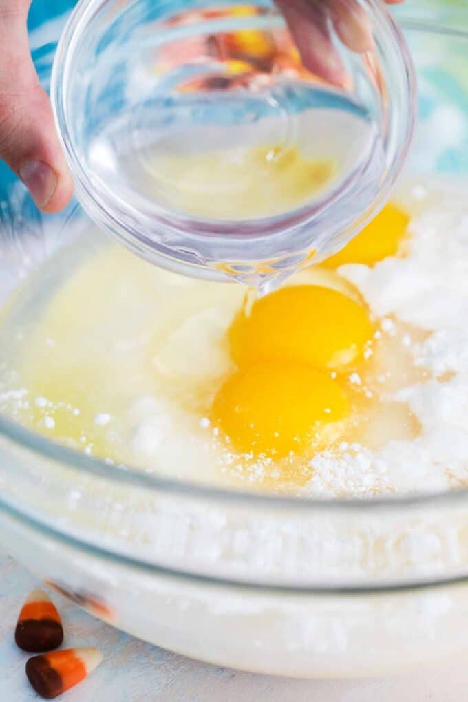 adding oil and eggs to cake mix in a bowl