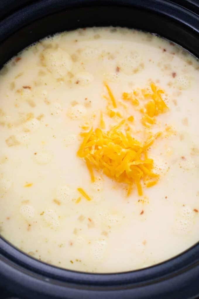 adding shredded cheese into slow cooker baked potato soup