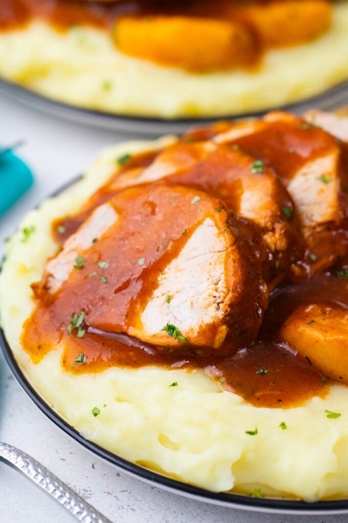 Sliced crockpot peach pork served over mashed potatoes.
