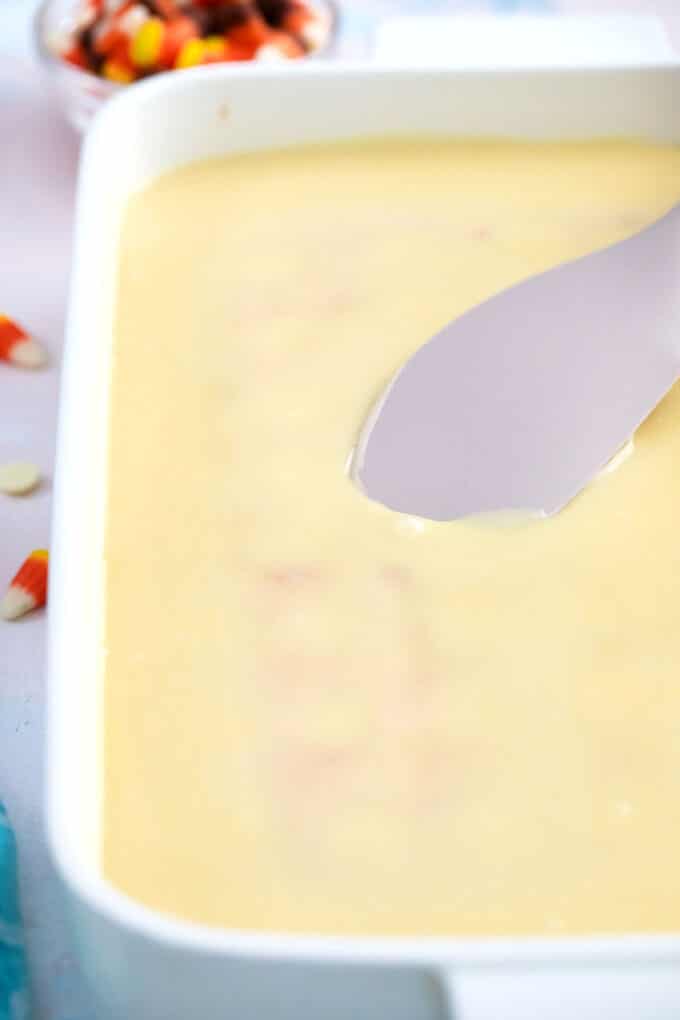 adding melted white chocolate mixture on top of a poke cake