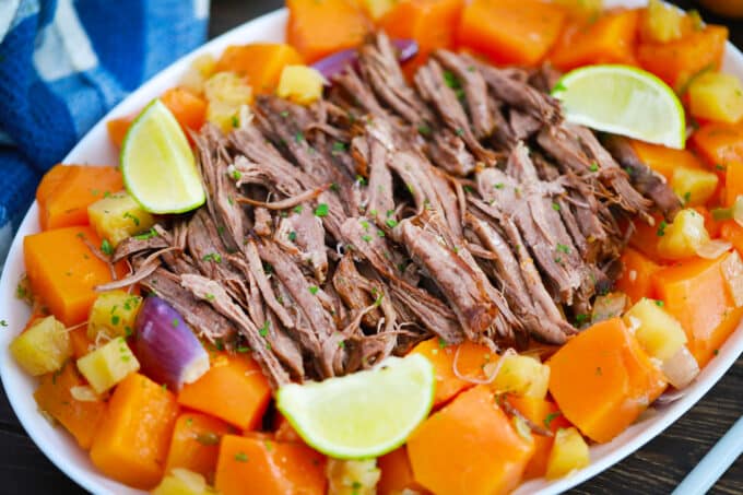 A serving plate with pumpkin pot roast and lime wedges.