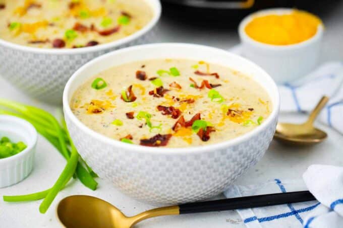 bowls of crockpot bacon ranch potato soup topped with shredded cheese and bacon