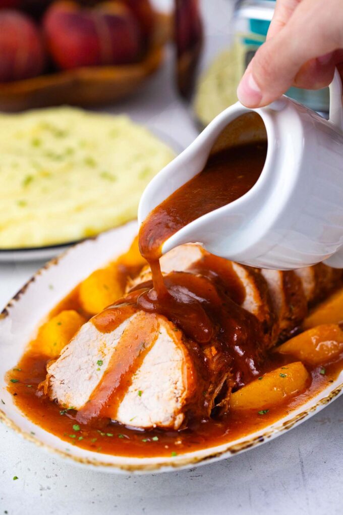 Pouring glossy sauce on top of sliced slow cooker peach pork.