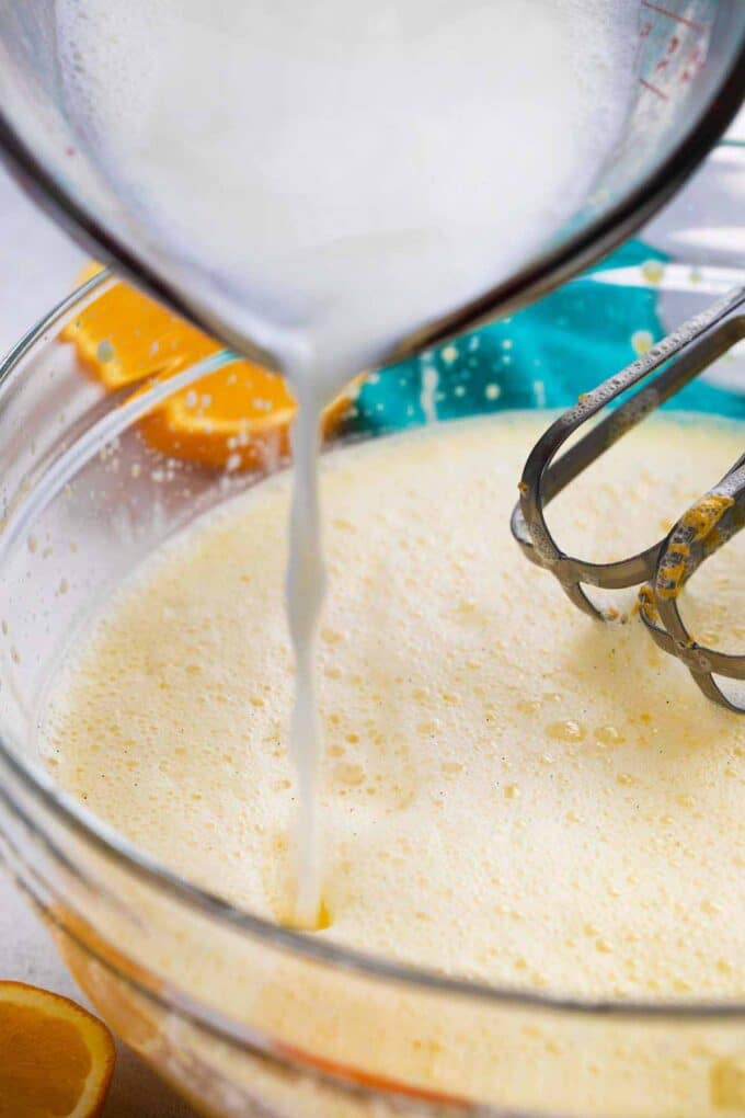 adding milk to a bowl with eggs to make orange custard