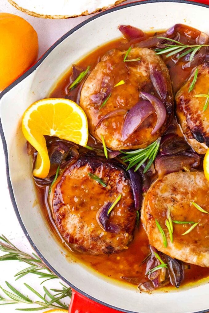 orange glazed pork chops with red onion and rosemary in a skillet