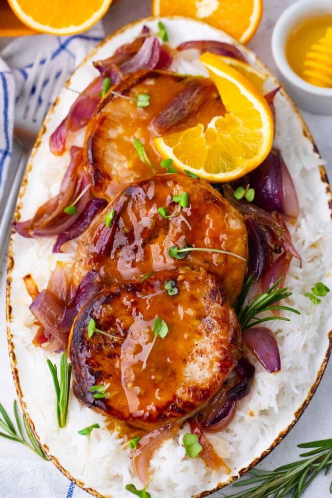 a platter of homemade orange glazed pork chops with red onion and rosemary on a platter of rice