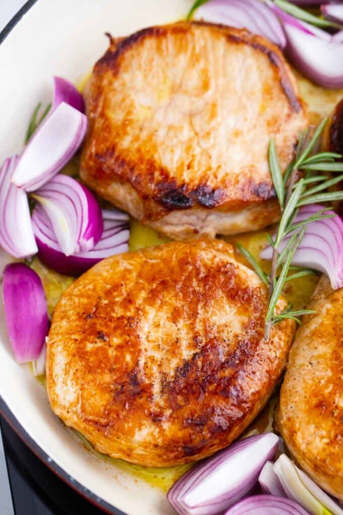 seared pork chops, red onion, and rosemary in a skillet