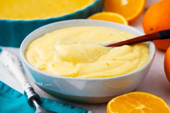 a bowl of orange custard with oranges next to it