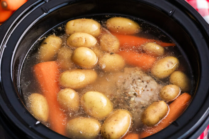 Adding veggies to cook in the slow cooker for corned beef.
