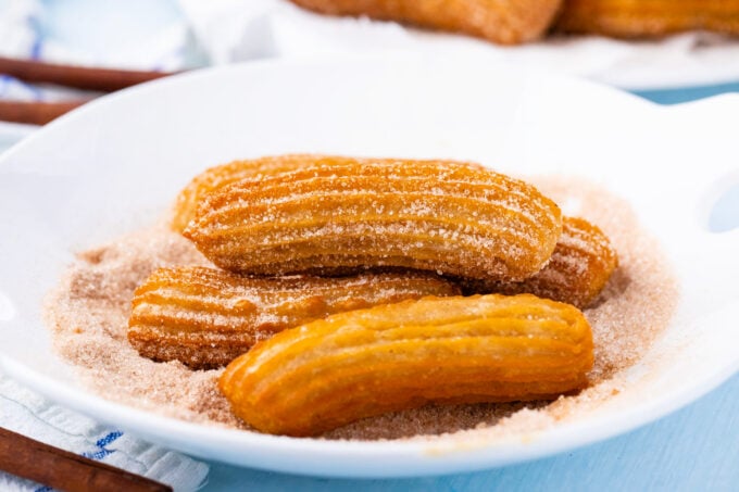 Coating churros in cinnamon sugar.