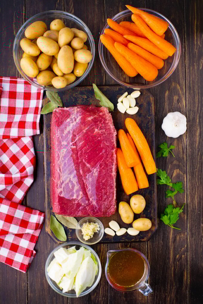 Overhead shot of slow cooker corned beef ingredients arranged on a wooden table.