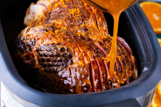 Pouring orange glaze over ham in the slow cooker.