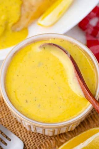 Overhead shot of a bowl with Bearnaise sauce and a small wooden spoon in it.