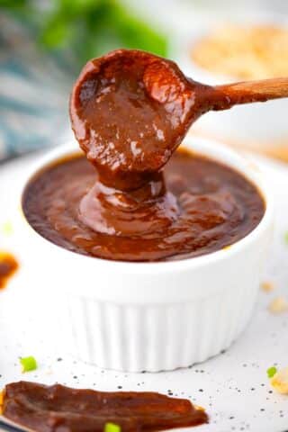 Creamy hoisin sauce dripping of a spoon into a ramekin.