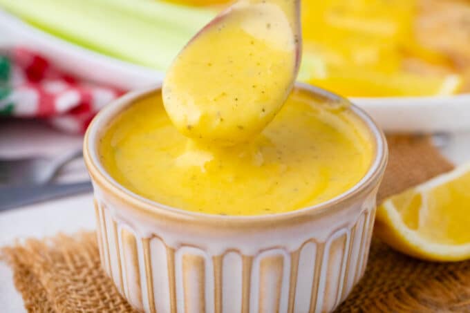 Homemade Bearnaise sauce dripping of a spoon into a bowl.