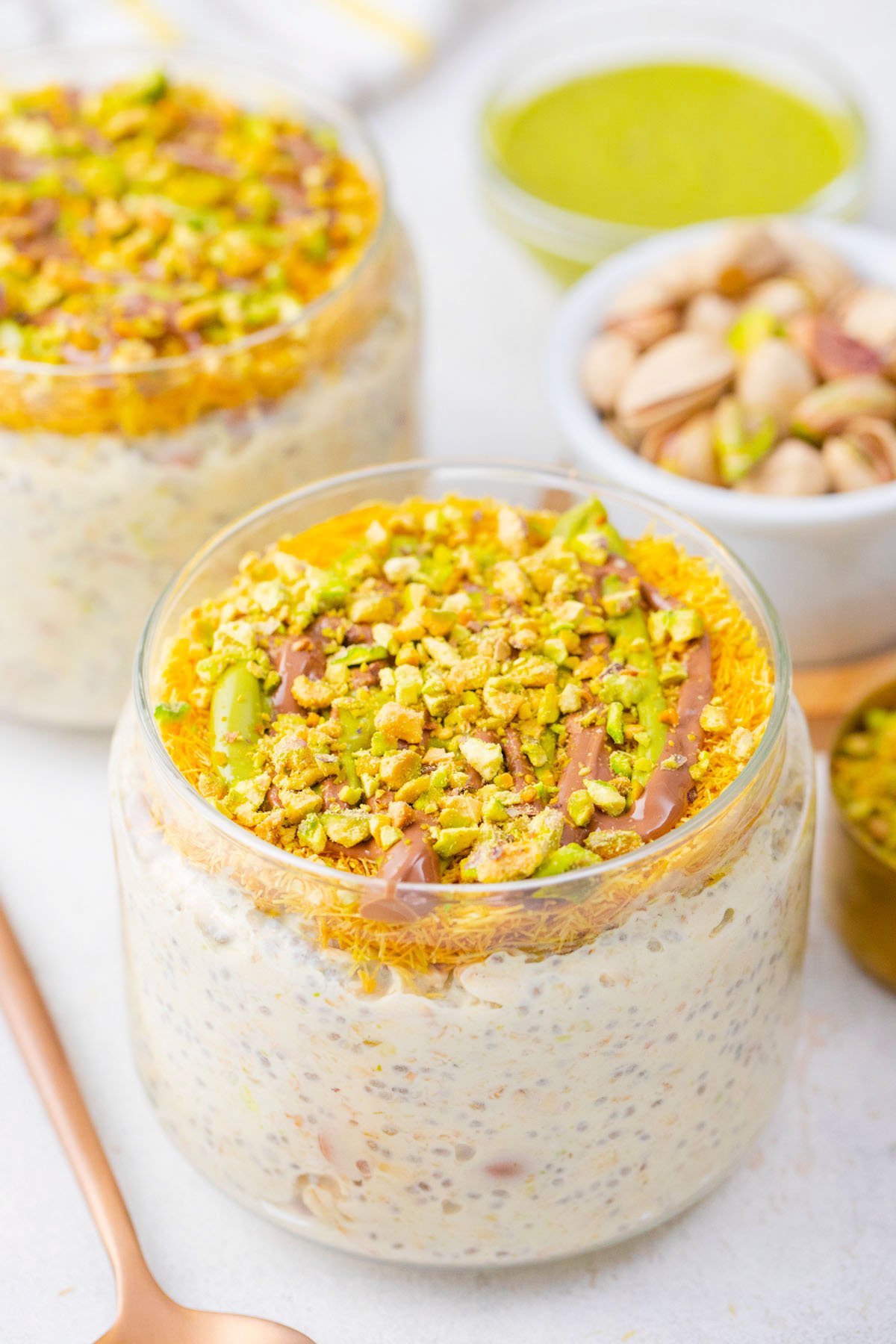 Jars of Dubai chocolate overnight oats topped with kataif, chocolate sauce, and chopped pistachios.