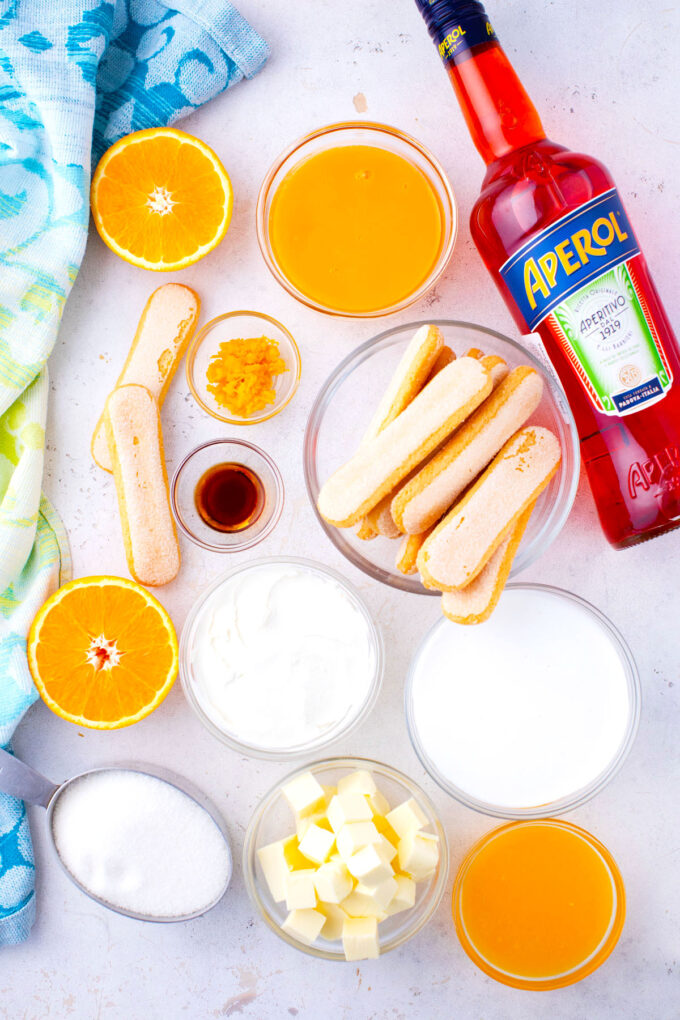 Overhead shot of Aperol spritz tiramisu ingredients in bowls on a light surface.
