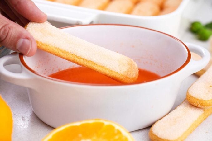 Dipping savoiardi cooking in a mixture of Aperol and orange juice.