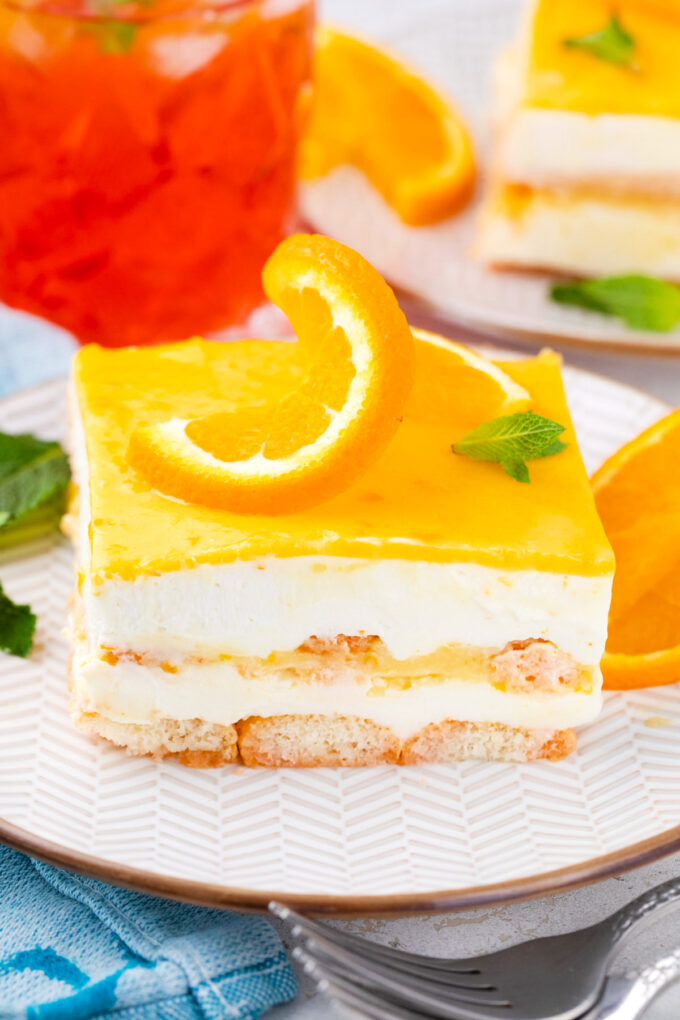 A slice of Aperol spritz tiramisu topped with orange curd and orange slices.