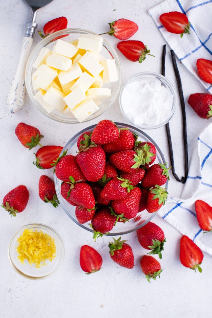 Overhead shot of fresh strawberry butter ingredients in bowls on a white surface.